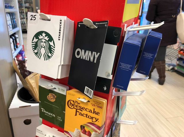 A display of gift cards, for Panera Bread and other brands, plus an open OMNY package on a retail display carousel